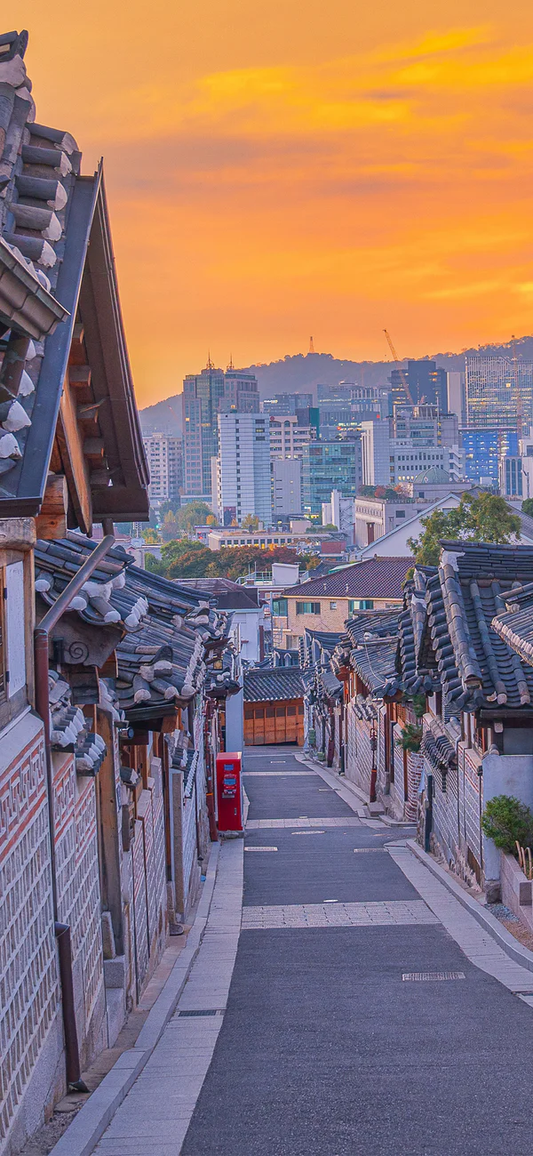 Solnedgång över Bukchon Hanok Village i Seoul, Sydkorea, med stadens silhuett i bakgrunden