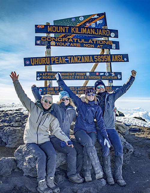 Familj sitter framför skylten vid Uhuru Peak på toppen av Kilimanjaro