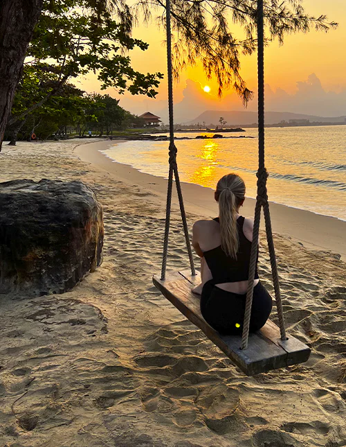 Person sitter på en gunga på en strand och njuter av solnedgången