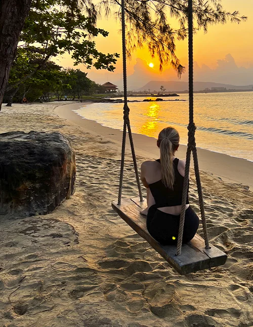 Person sitter på en gunga på en strand och njuter av solnedgången
