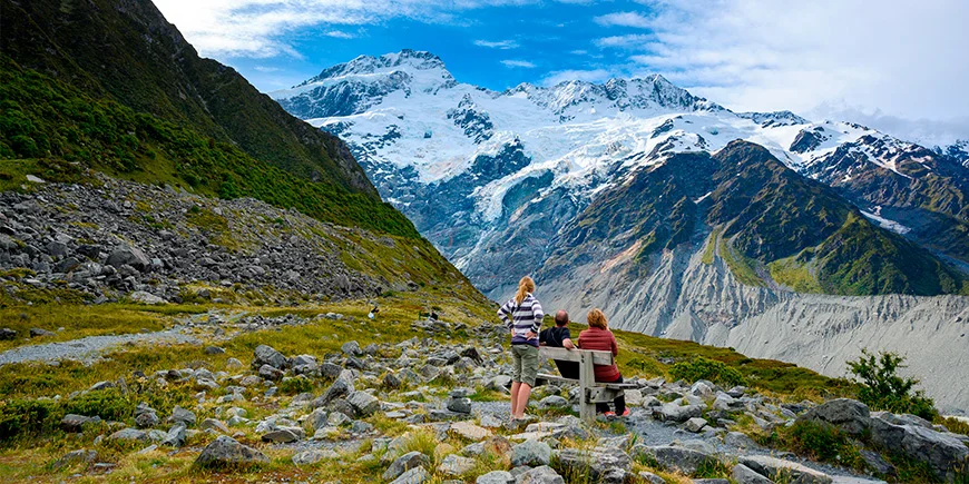 En familj på tre personer tittar på bergen från utsiktsplatsen Kea Point i Mount Cook Nationalpark