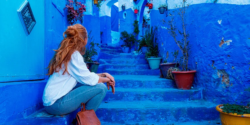 Kvinna sittande på trappan i den blå staden Chefchaouen, Marocko
