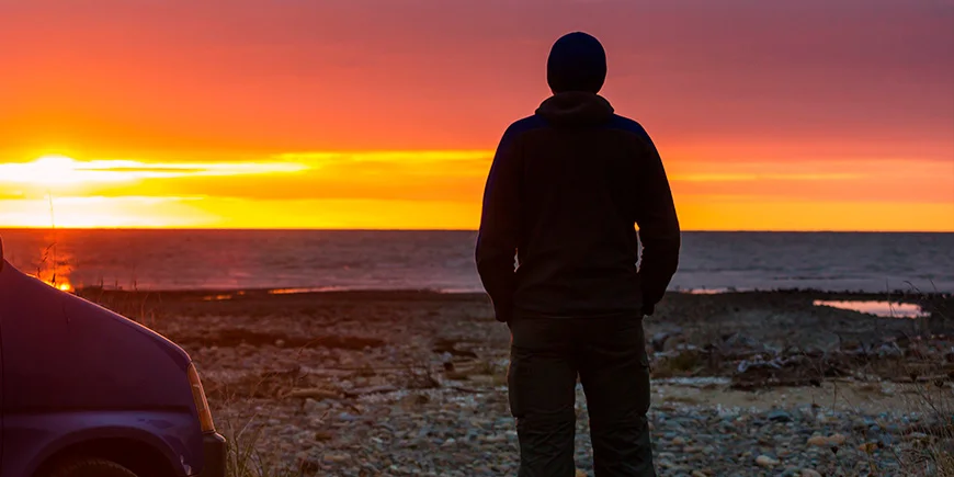 Man njuter av solnedgången vid vattnet i Nya Zeeland