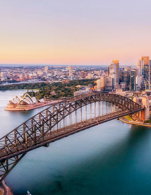 Flygfoto av Sydney Harbour Bridge badad i ett lila sken.