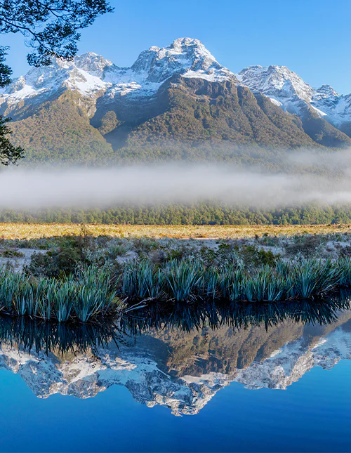Mirror Lake, lågt hängande dimma och snötäckta bergstoppar en klar vinterdag i Milford Sound, Nya Zeeland