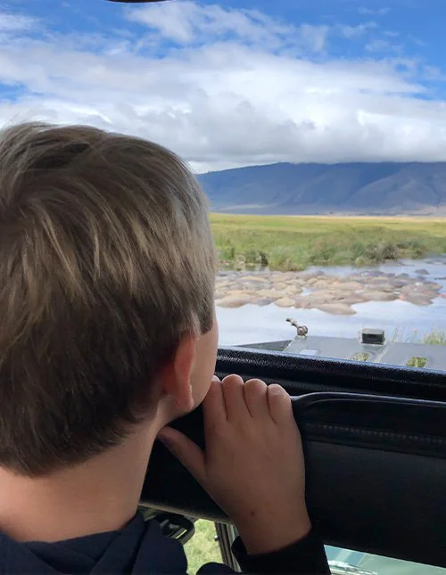 Ett barn tittar ut från en safaribil mot en flod och savannen