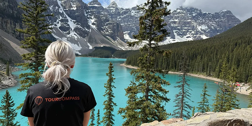 Kvinna i TourCompass-T-shirt som blickar ut över vattnet vid Lake Louise i Kanada